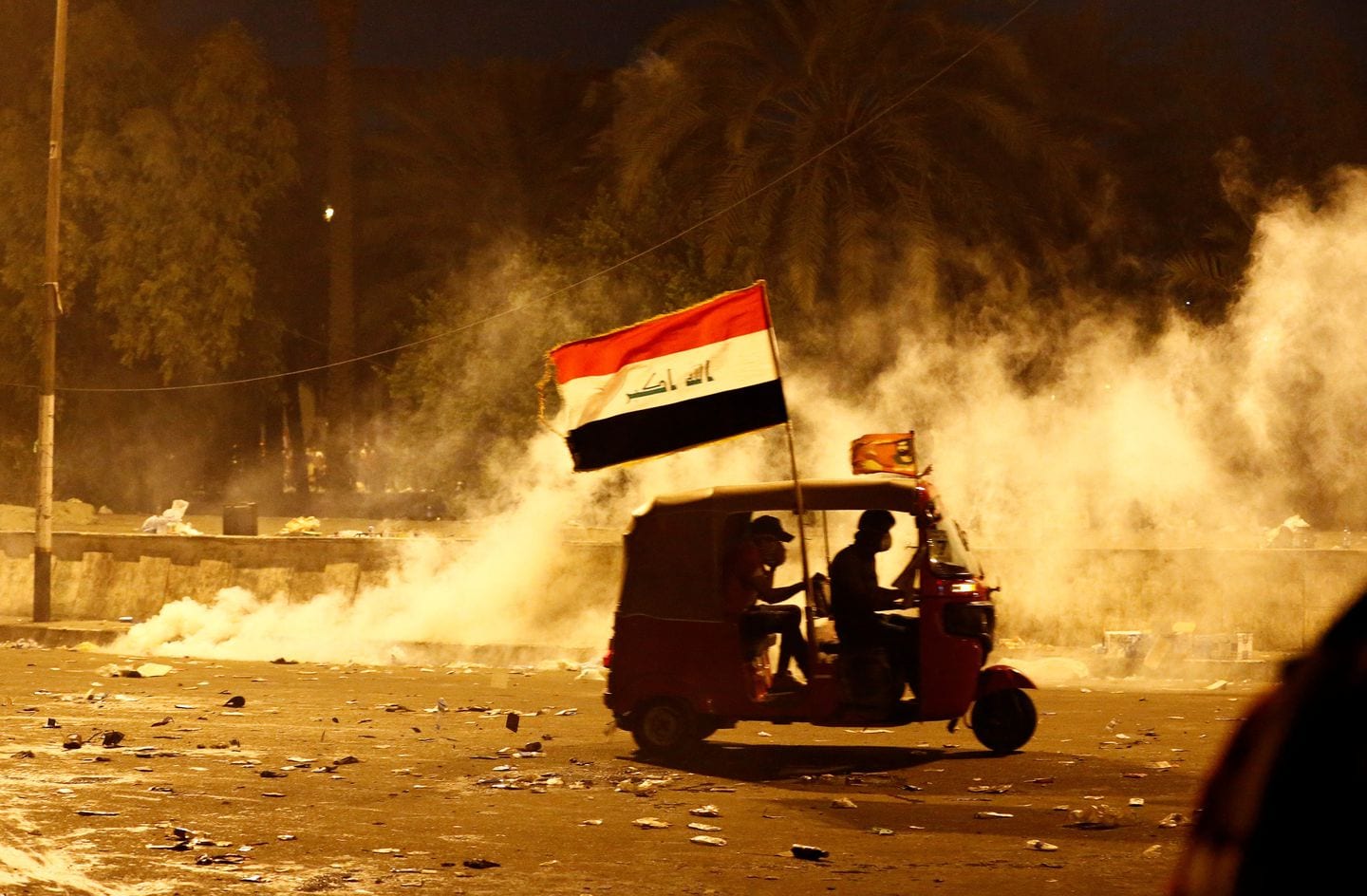 A tuk-tuk speeds away from tear gas fired by Iraqi security forces. (Thaier Al-Sudani/Reuters)